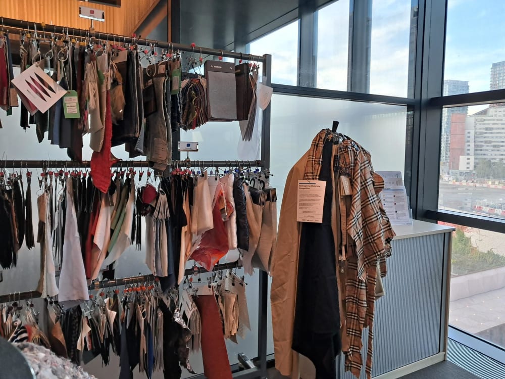 Mannequin with clothes draped on, next to hanging rails of fabric samples. 
