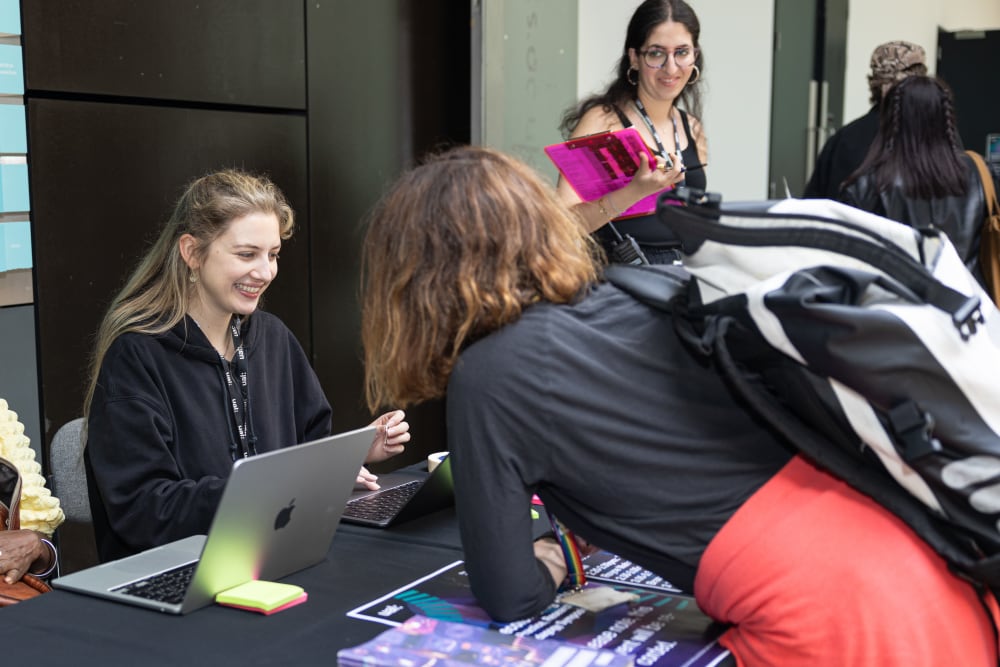 Smiling woman at welcome desk, greeting guests. 