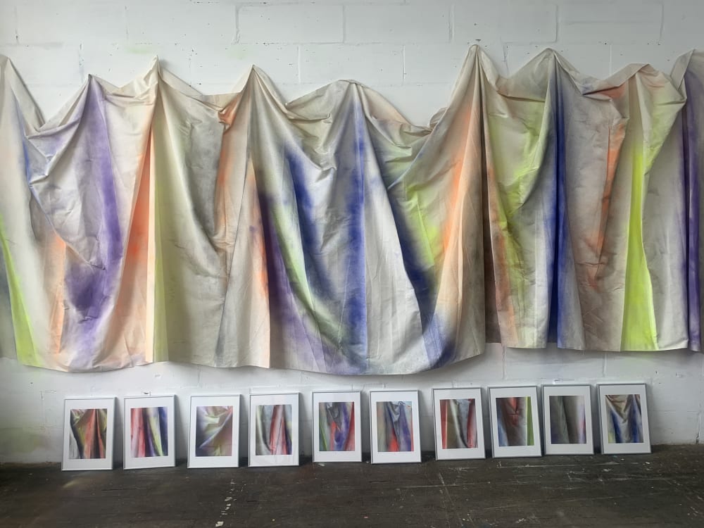 Canvas hanging on a white wall. The canvases been sprayed with blue, orange, purple and yellow paint. 