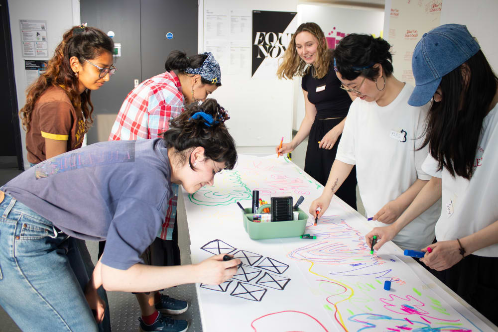 A group of people stand over a table, smiling as they draw