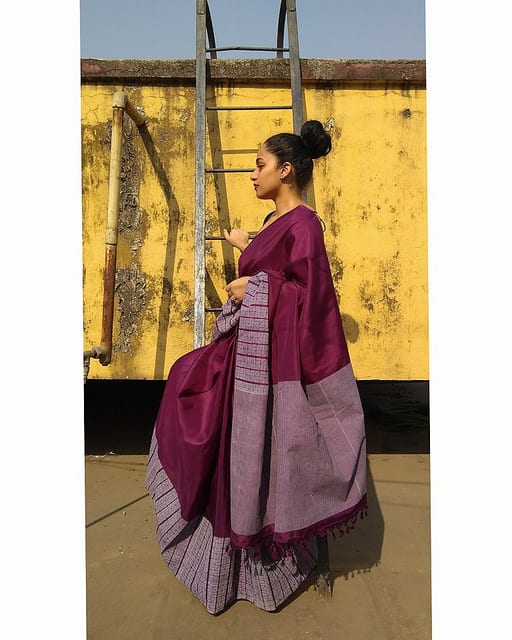 A woman modelling a long purple dress against a yellow wall.