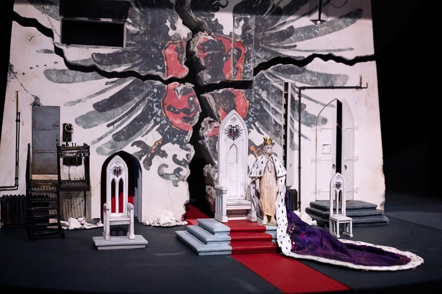 A set design featuring a red carpet leading to a throne up some stairs.