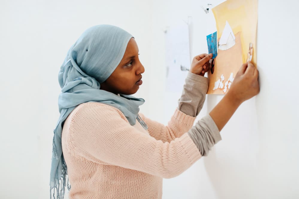 Image of woman with a headscarf hanging a drawing on the wall
