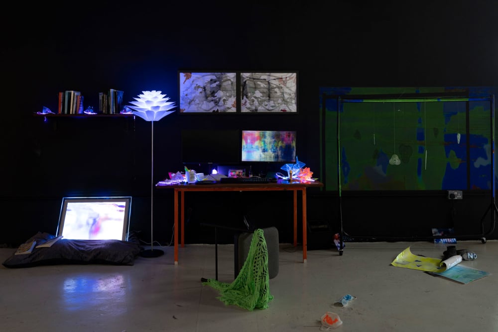A dark room with a large art installation in it comprising of a table, screen, shelves and other objects, many lit with LED bright white lights.