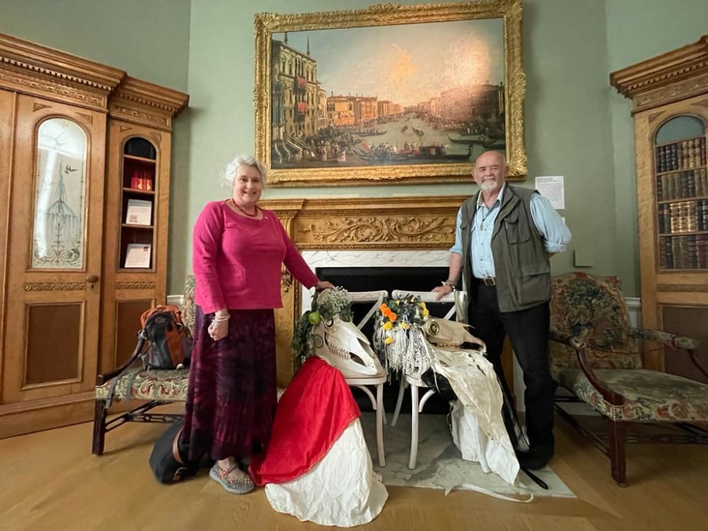 line up of John and Sue Exton in front of period fireplace with folk costumes on floor