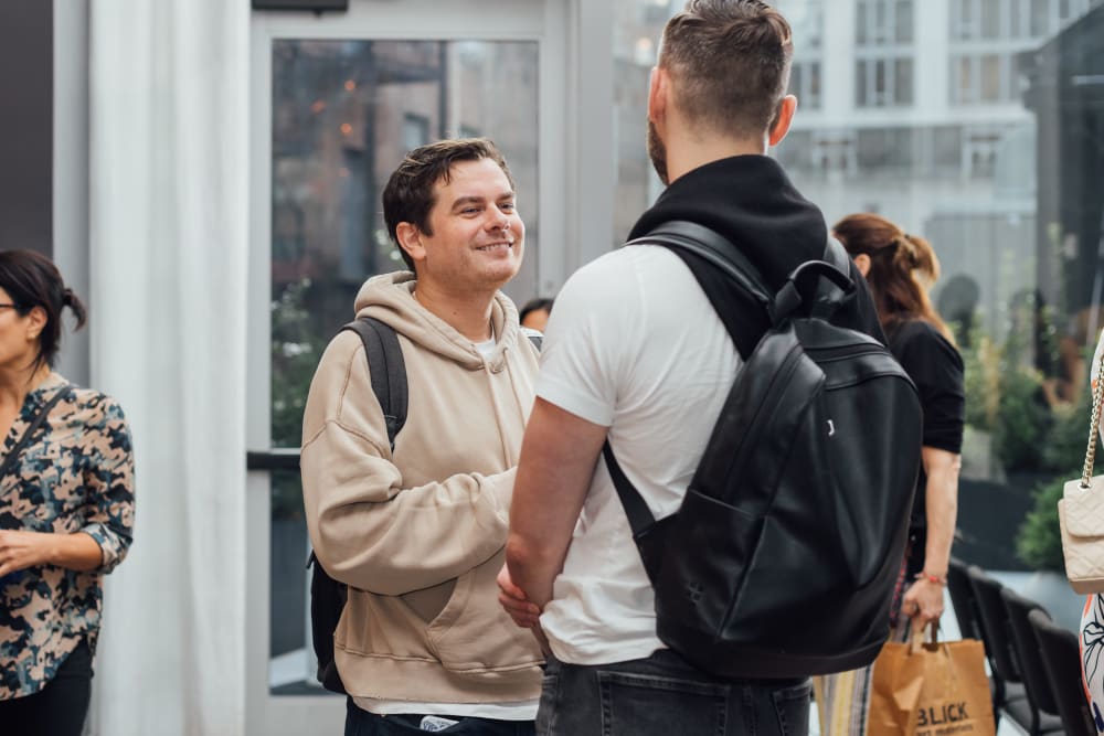 2 guests chatting; one man is facing the camera and smiling, the other man has his back to the camera.