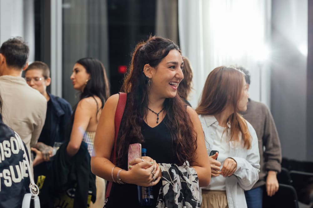 A woman smiling and looking off to the left. She's got a black and white jacket over her left arm 