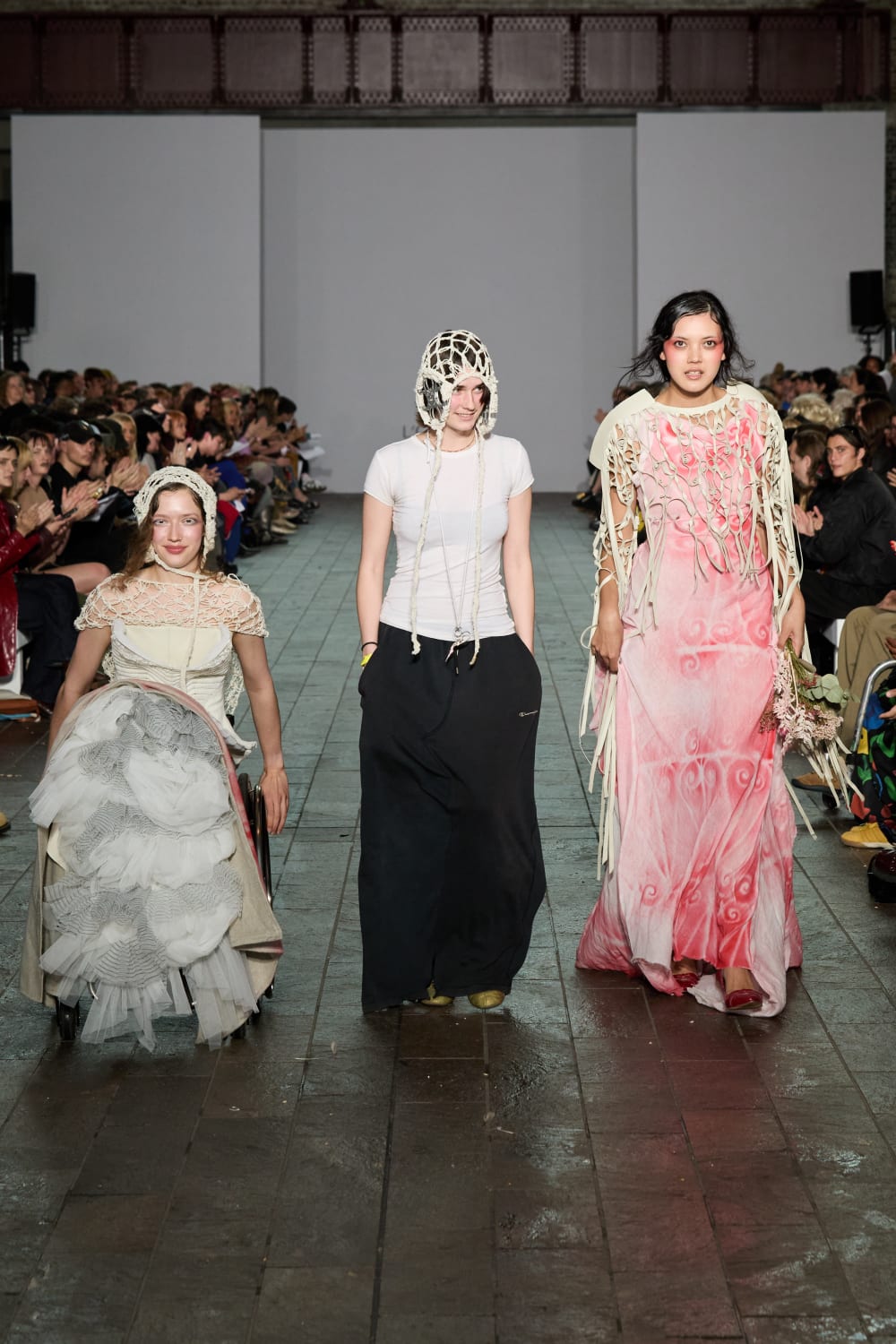 Two models and a designer walking on a catwalk.