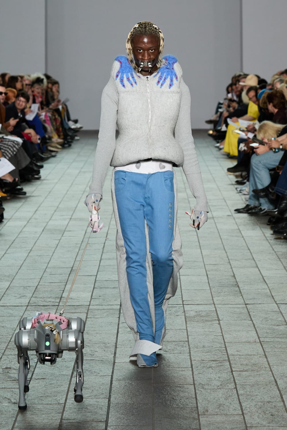 Image shows a black male model walking the catwalk with a robotic dog.