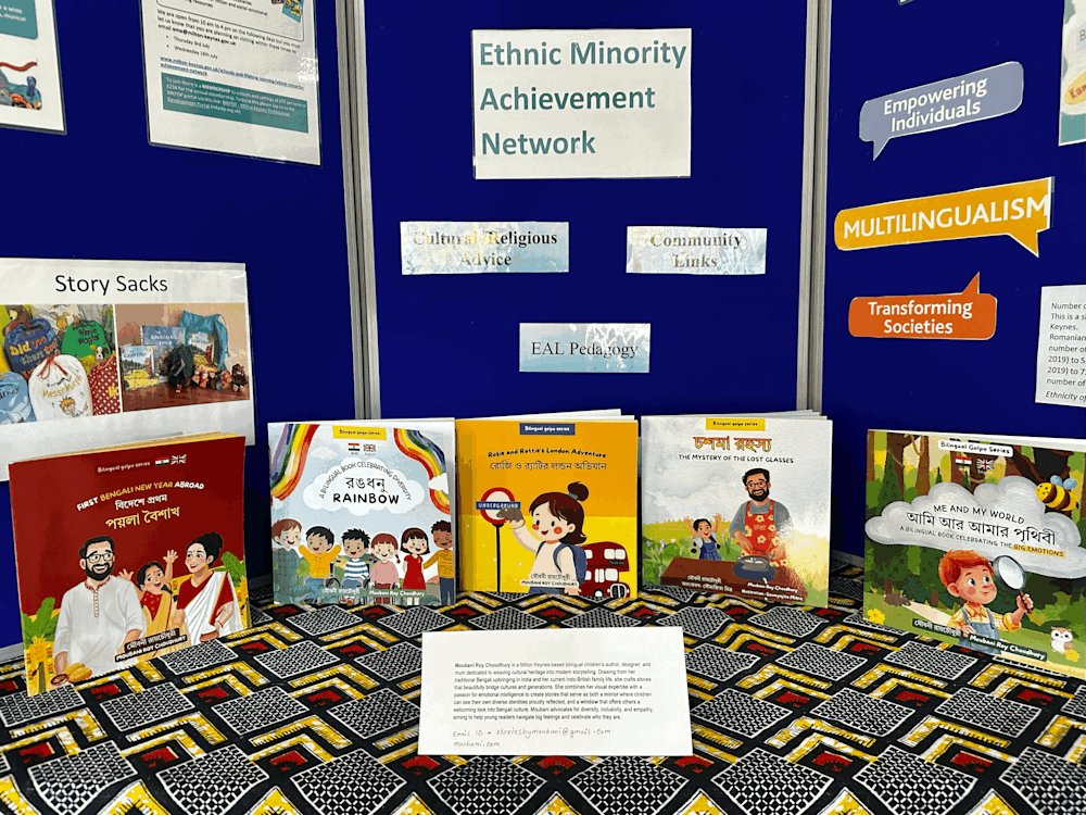 Display of bilingual children’s books by Moubani Roy Choudhury at an Ethnic Minority Achievement Network stand, featuring titles in Bengali and English alongside educational and multilingual resources.