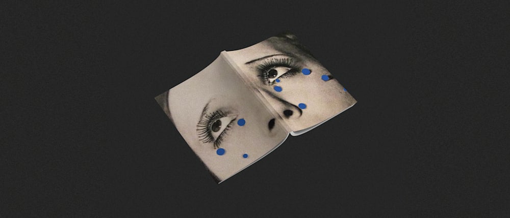 A book with a face printed, the eyes look upwards with blue circular sparkles around the face