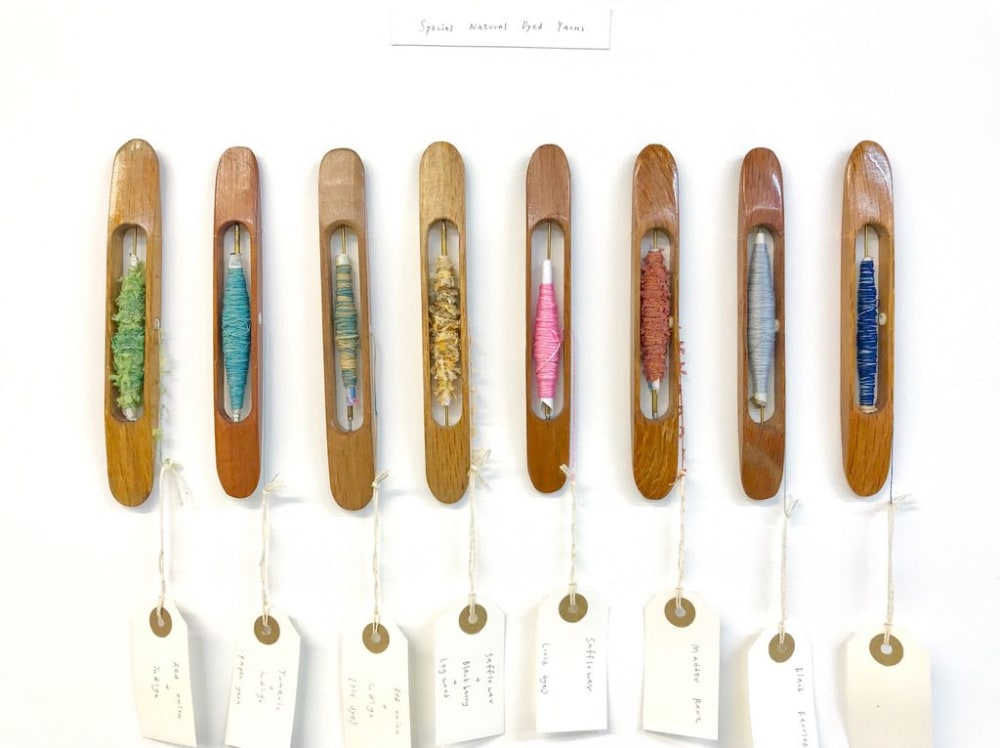 Different colourled threads presented on the wall in wooden vessels with description tags attached.