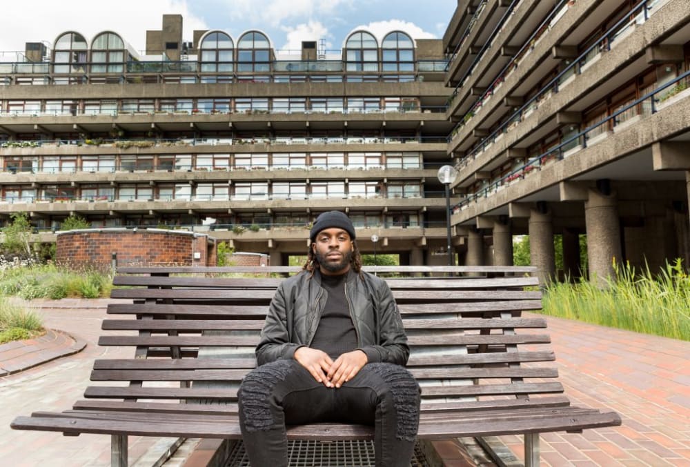 a portrait of a person sitting on a wooden bench at the barbican