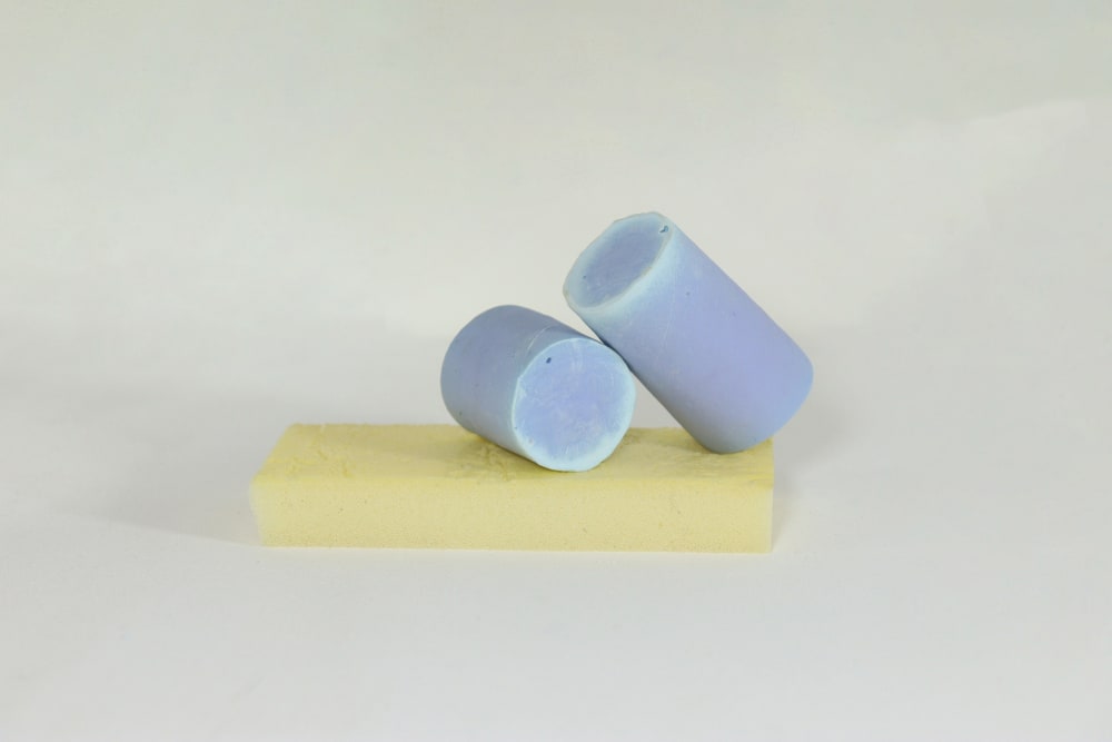 2 blue cylinder-shaped sculptures resting on a light-yellow foam rectangle