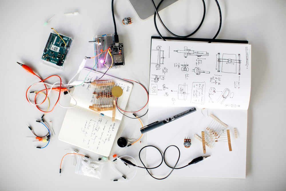 A flatlay of notebooks, wires, pens and switchboards, all relating to creative computing.