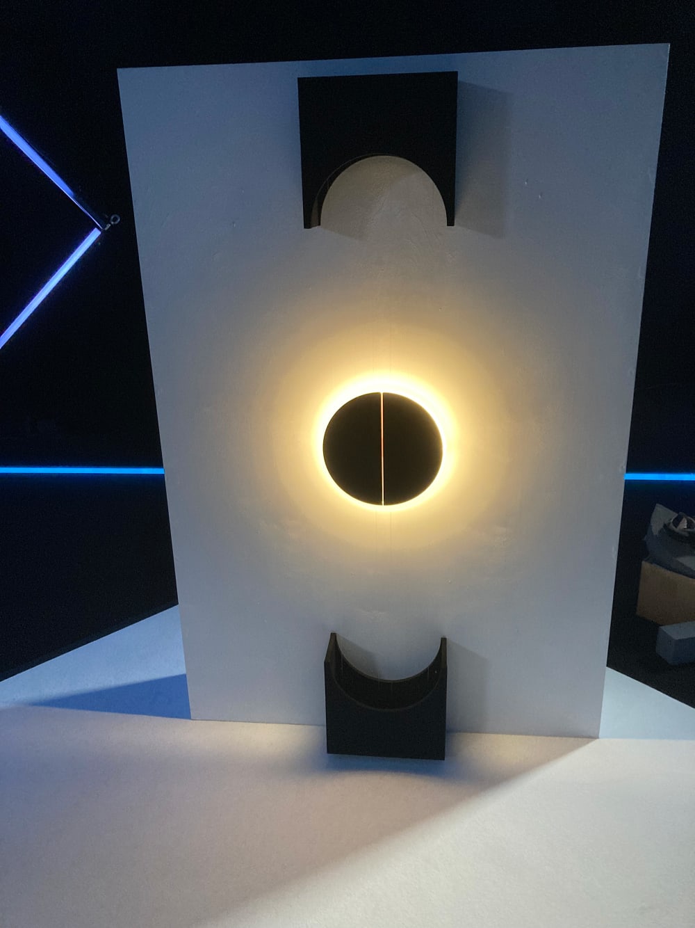 Black and white sculpture with geometric shapes and a central ring of yellow light 