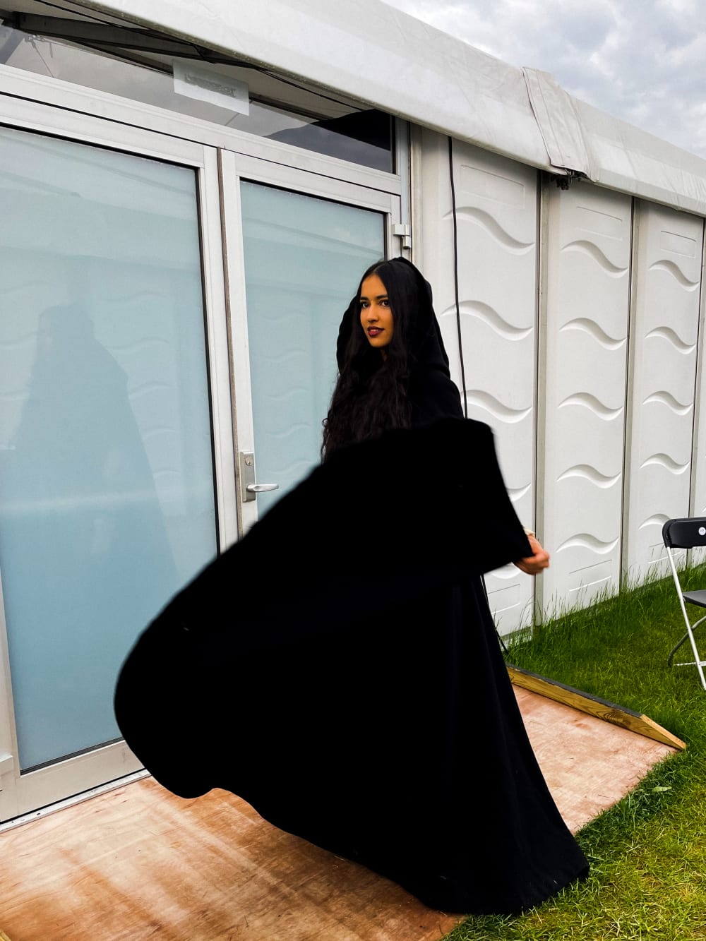 A performer in a black robe poses in front of a trailer 