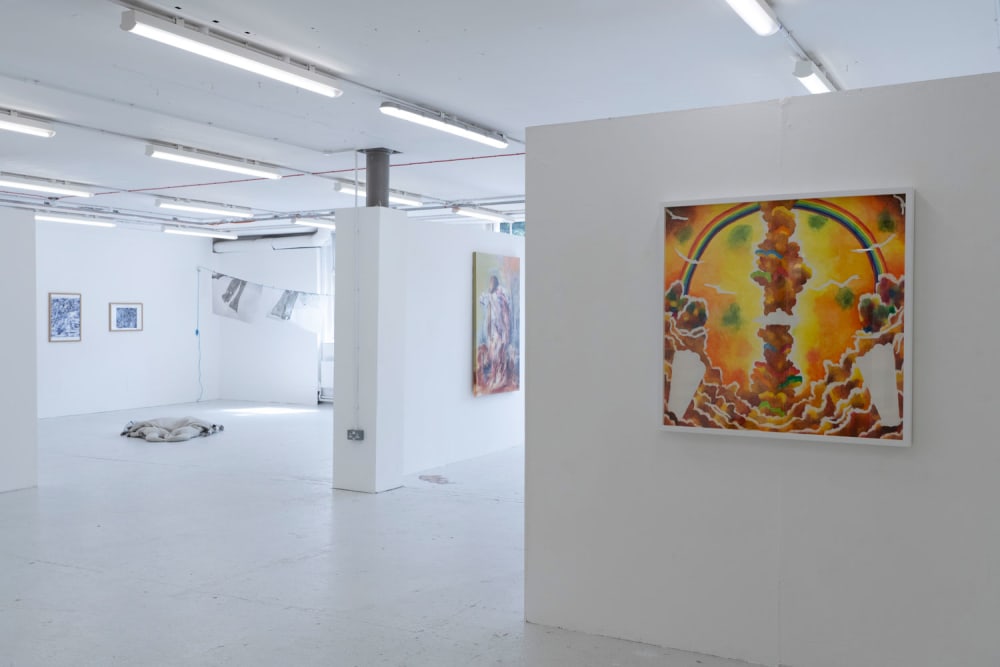 A white-walled gallery space flooded with natural light. Paintings are hanging on all the walls.