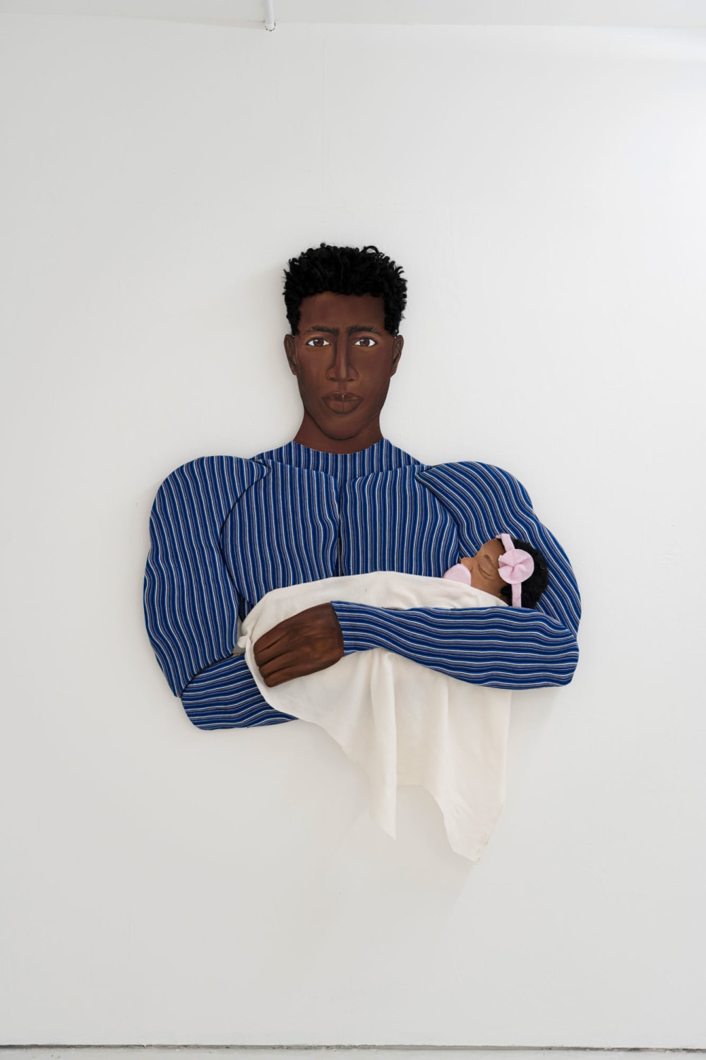 A 3D sculptural painting of a man in a blue and white striped shirt holding a baby in a white blanket with a pink flower headband.