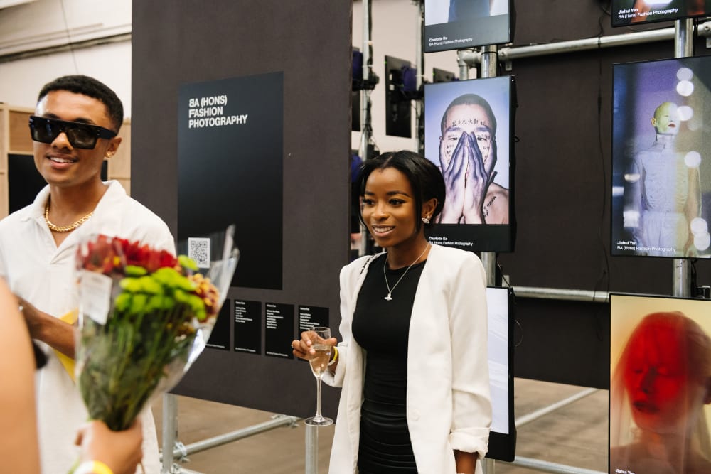 Fashion photography student with drink in hand and friend in front of work