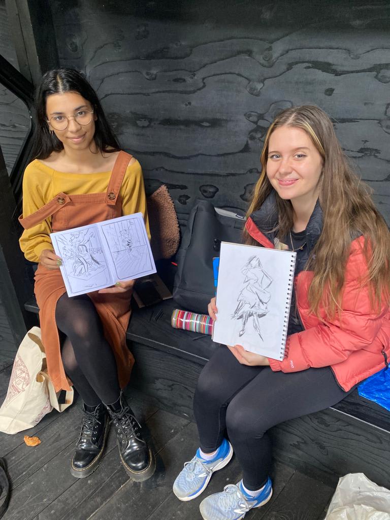 two students showing their illustrations of women to the camera