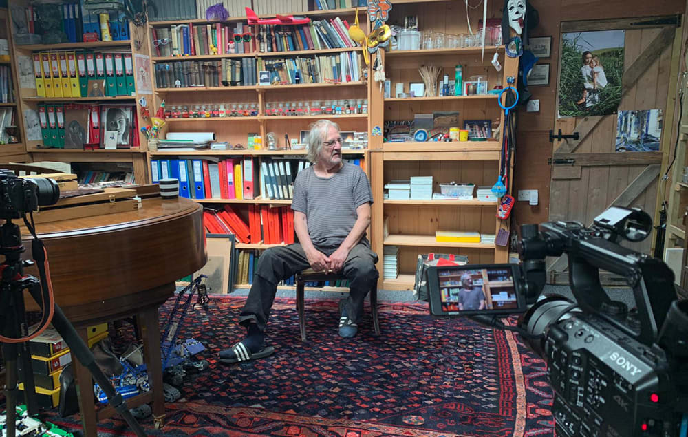 Still of an interview in progress with a man sitting in front of bookshelves.