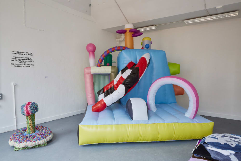 A large inflatable and colourful sculpture, there is a warning sign on the left asking not to climb the sculpture
