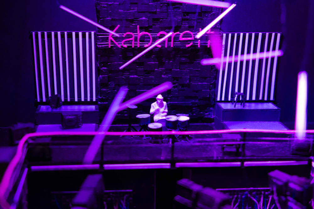A purple model of a club, where the drummer is playing alone. The name of the club reads: 'Kaberett'
