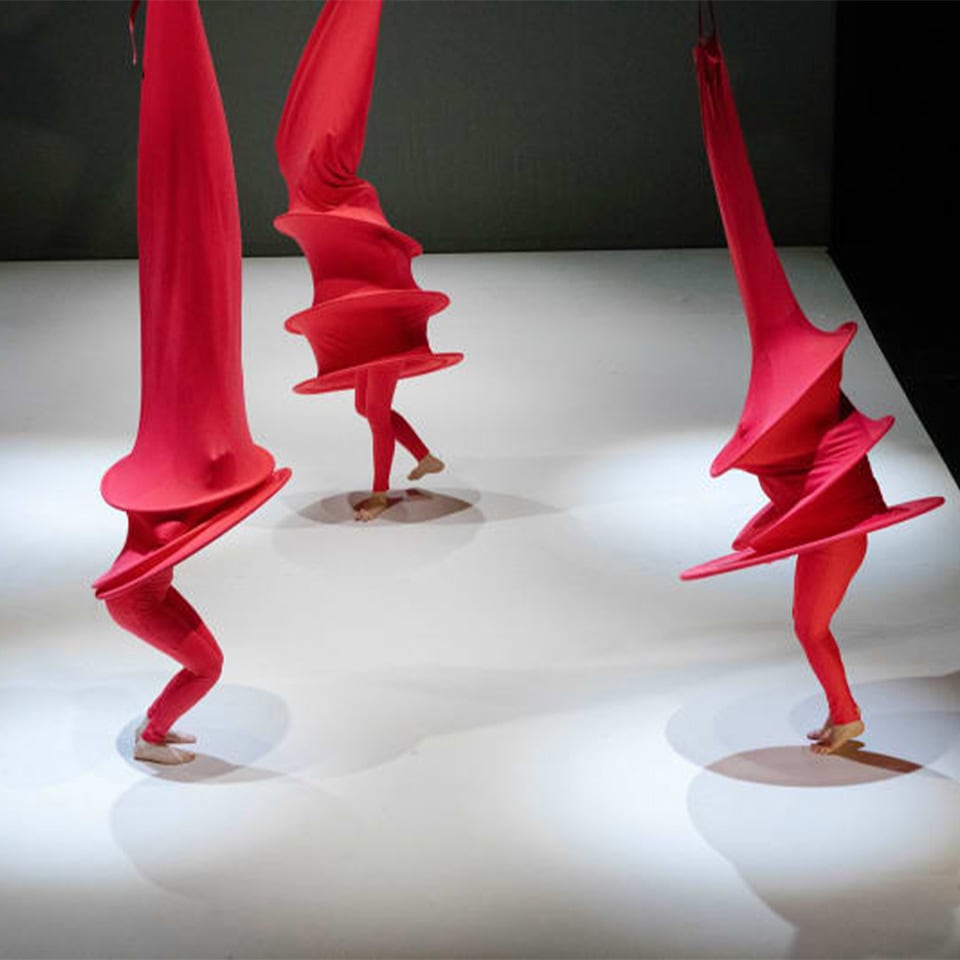 three performers dance on stage with red costumes on