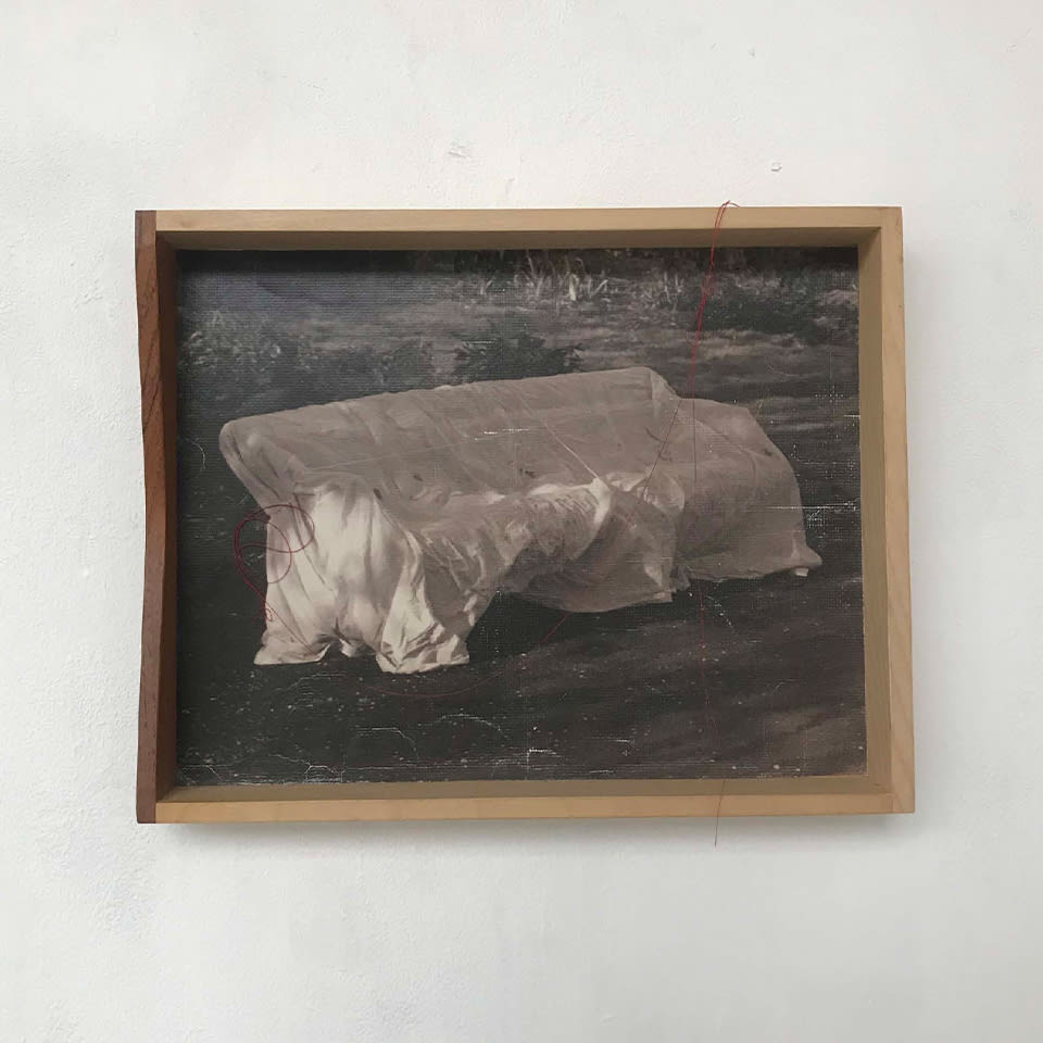 A framed photograph of a bench draped in fabric hangs on a white wall. 