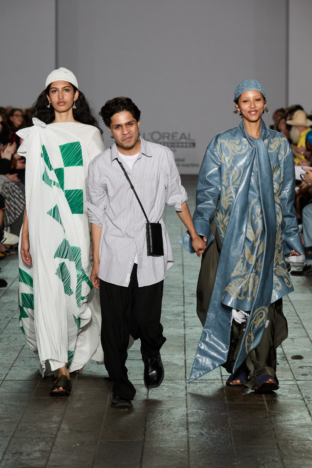 Two models and a designer walking on a catwalk.