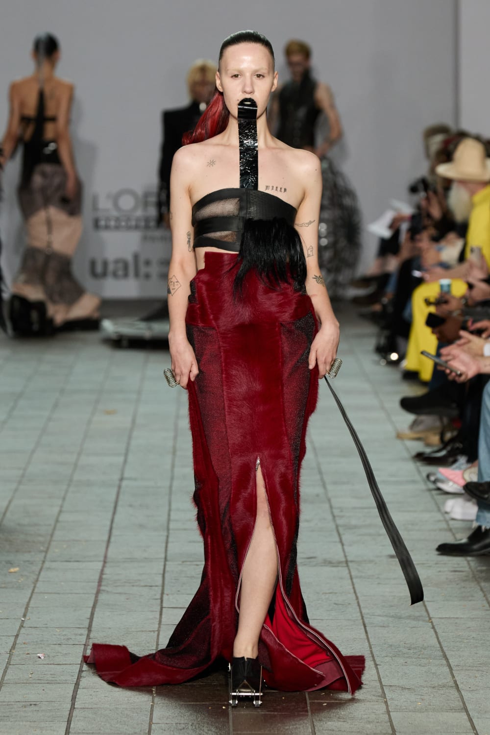 image shows a model wearing gothic like makeup , a long deep red skirt and a piece of black material that hangs like a tongue from her lips.