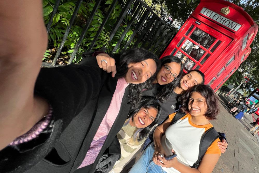 Group selfie of a cohort of students with a London red telephone box in the background