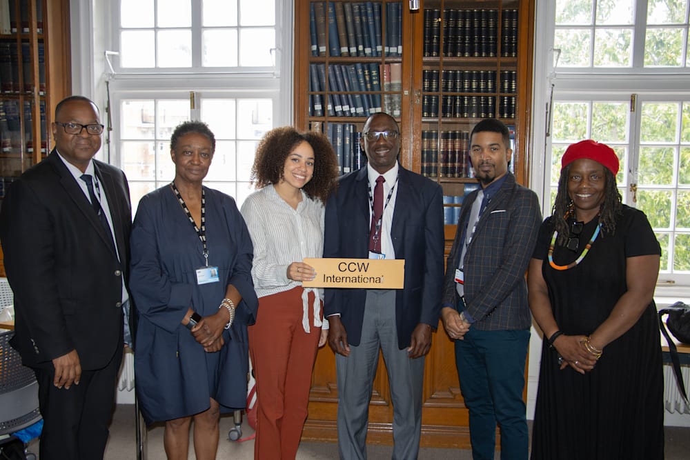 A row of academics from Chelsea, Camberwell and Wimbledon and University of West Indies, holding up a sign with the wording CCW International 