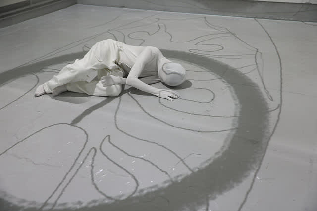 Figure all in white with their face covered laying on the floor.