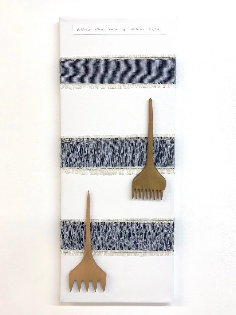 A white and blue weaving with two wooden gardening tools on top.