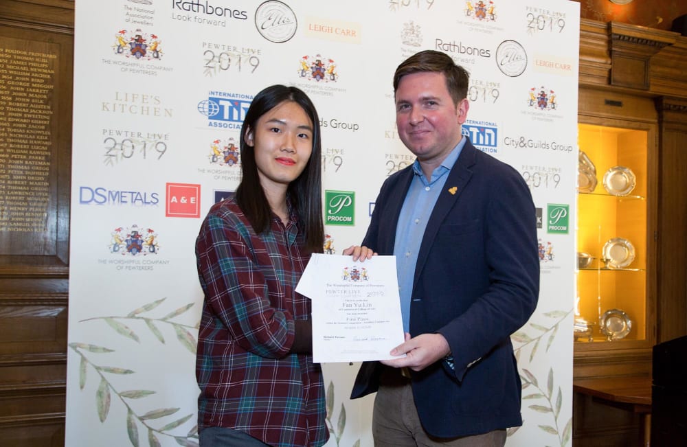 A woman and a man pose for a photos with a certificate against a white backdrop.