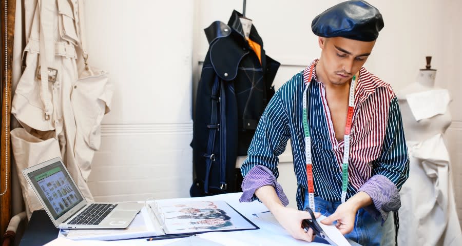 Student in studio cutting fabric in front of a laptop.