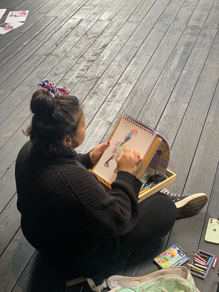 student sat on the ground drawing on an easel 