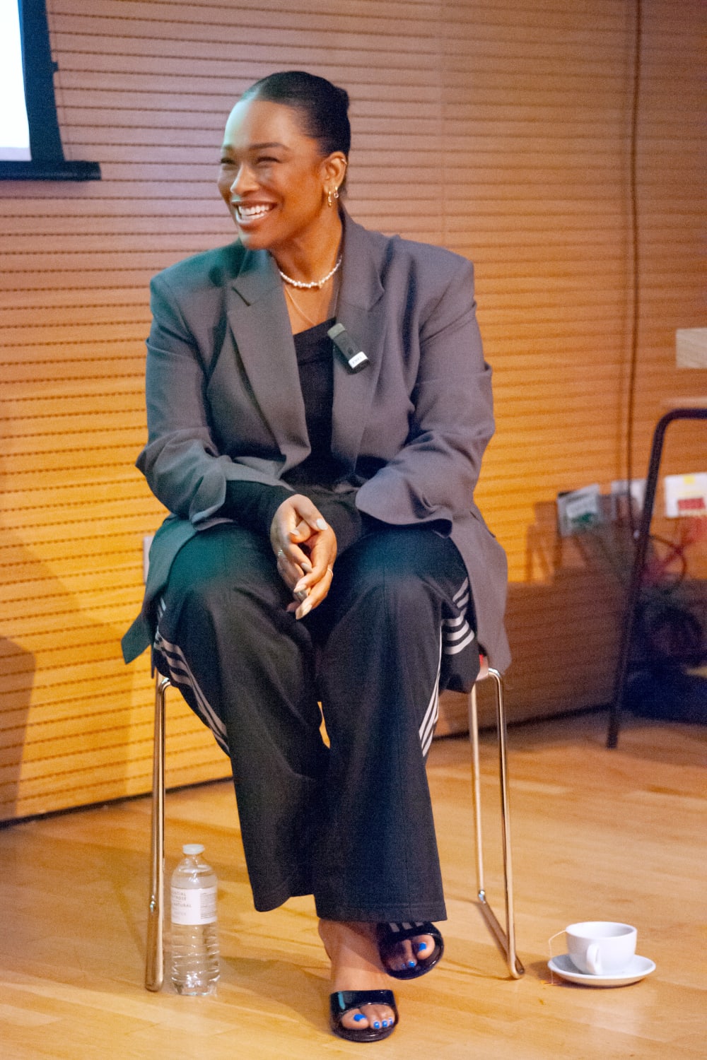 Sharmadean smiling. She's wearing an oversized grey suit and slip on mules. 