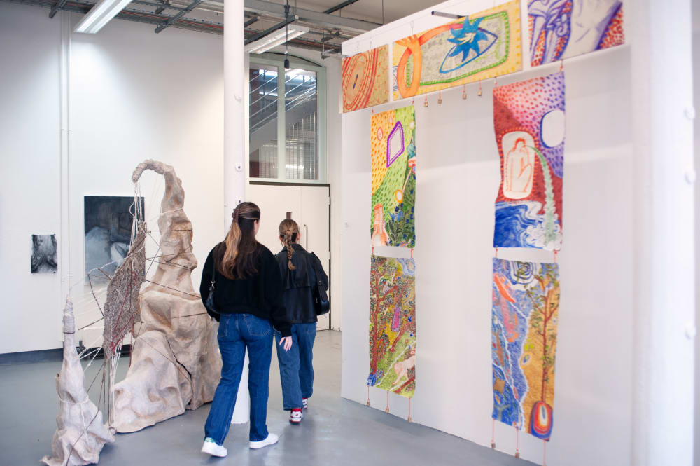 Guests walking around the exhibition. On the left is a sculpture and on the right is a series of paintings hanging in an archway formation.
