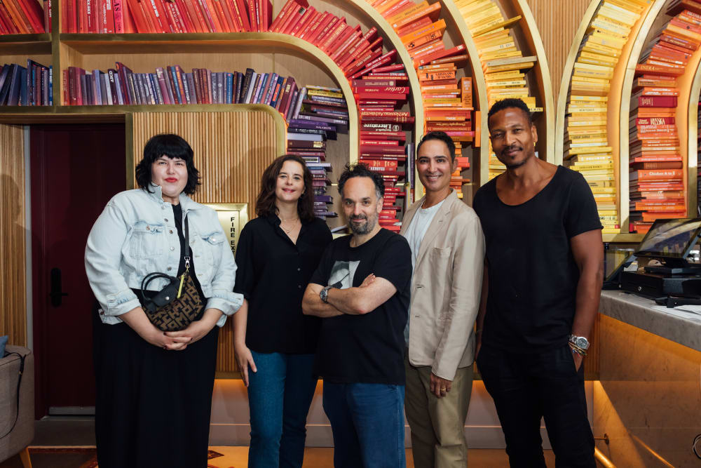 Members of the committee standing together. The wall behind them is wood panel with curved bookshelves. 