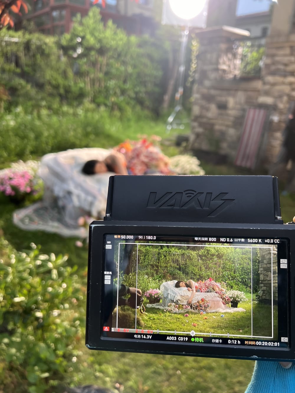 camera lens showing a woman draped in flowers lying down in a garden