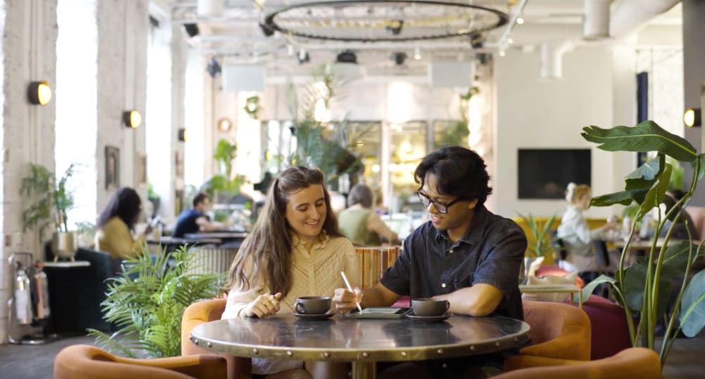 Vince Ibay and Jessica Miller sit at a table collaborating and drawing on a tablet. Others work in the background.