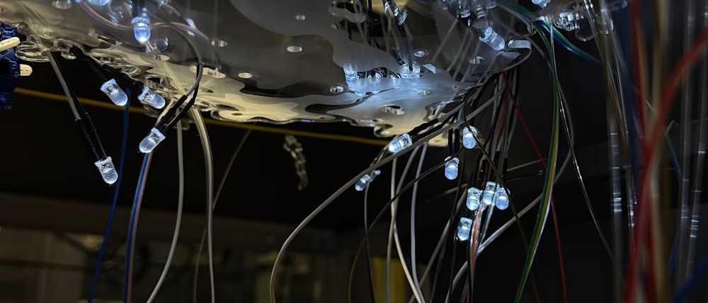Close-up of tangled colored wires and tiny glowing LED bulbs beneath a reflective surface, creating a dark, intricate, futuristic scene.