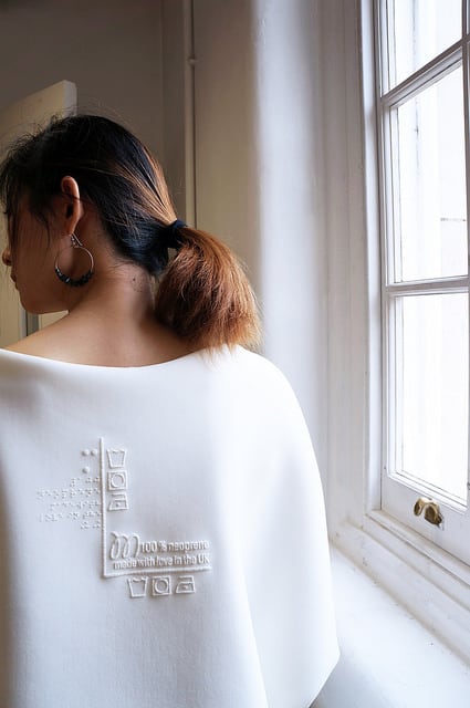 A model wearing a white jumper with braille on the back.