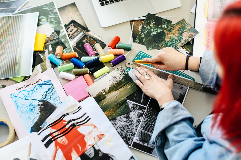 Aerial shot of woman's hands cutting paper with cotton reels, magazines and other studio work in progress