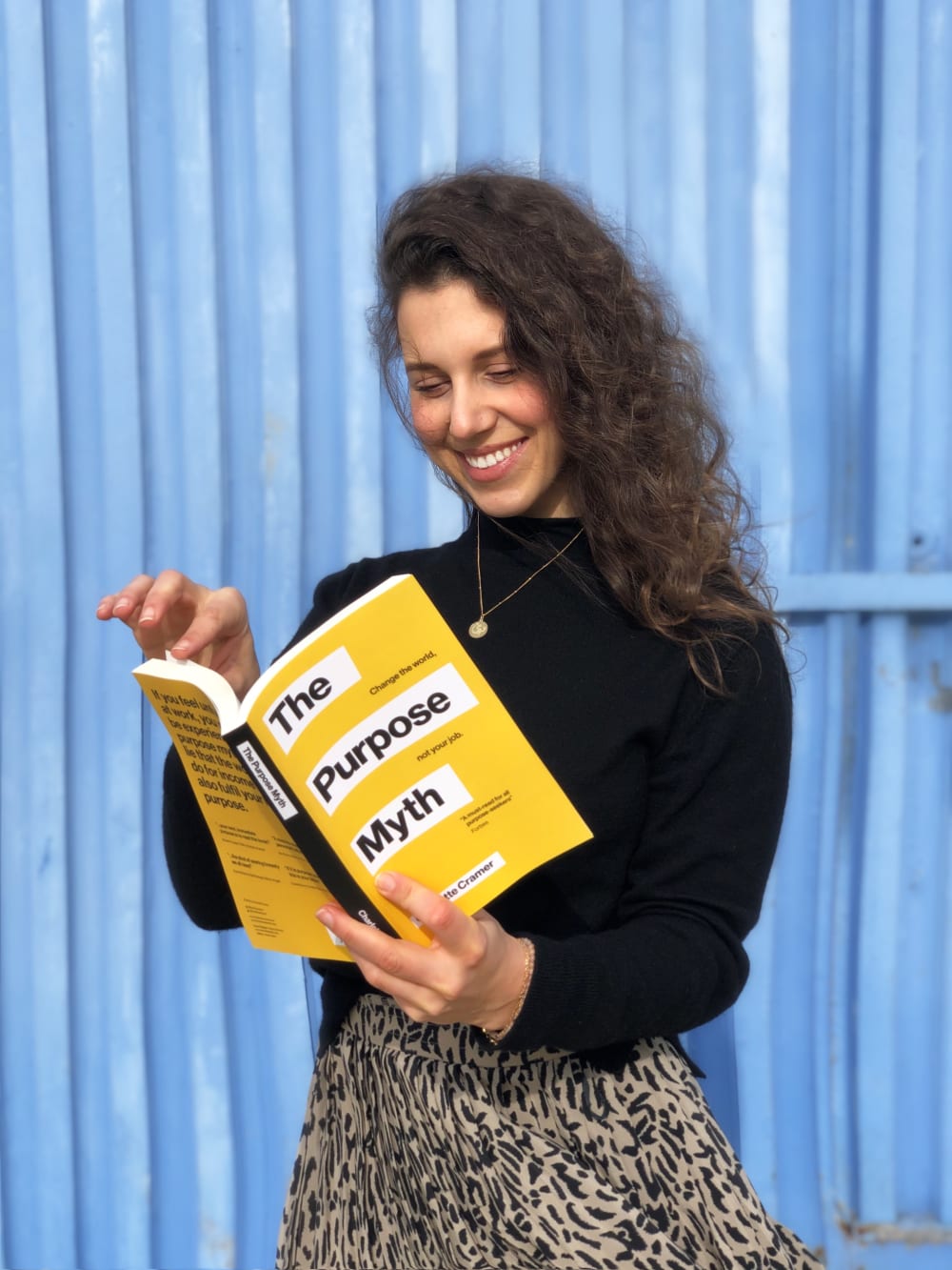 Woman reading a book. The book cover is yellow, titled 'The Purpose Myth'