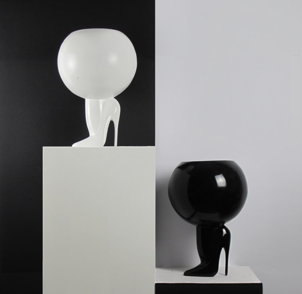 contrasting black and white heeled shoes with  a large spherical design on top, placed on black and white plinths
