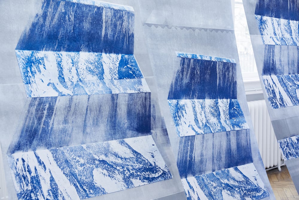An installation of prints, blue textural prints, hung in structural shapes.   